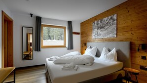 A modern bedroom with a large bed, wooden paneling, a window with curtains, a bench, and a painting on the wall. - 59315 Steinadler 315 T S (Gargellen)