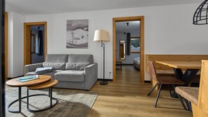Una sala moderna con un sofá gris, una mesa de centro redonda de madera, una lámpara de pie y un comedor con sillas y una mesa de madera.