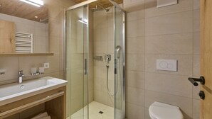 A modern bathroom with a glass-enclosed shower, a white sink, and a toilet.