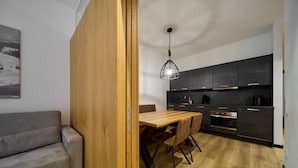 Une cuisine moderne avec des meubles de couleur sombre, une table à manger en bois et un luminaire suspendu.