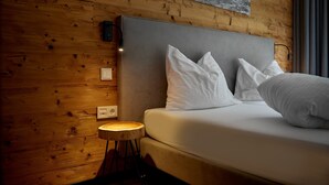 Une chambre avec un mur en bois, un lit avec une literie blanche et une petite table ronde avec une lampe.