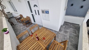 Une table et des chaises en bois sont disposées sur un balcon, près d’une porte blanche et d’une plaque portant le numéro « 79 ».
