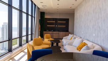A modern interior with large windows, a sofa set, a dining area, and a kitchen.