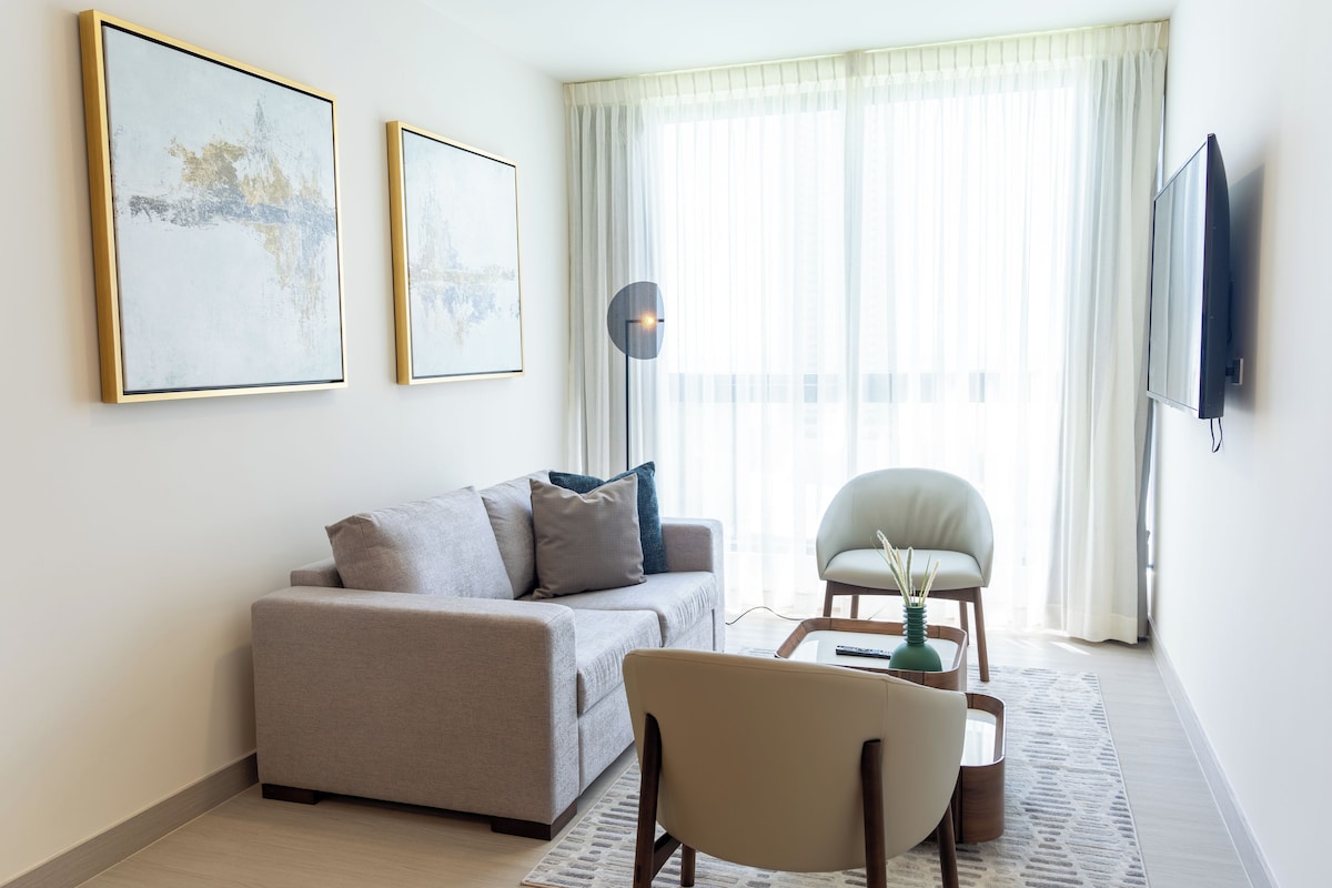 Un salon comprenant un canapé, un fauteuil, une table basse, un lampadaire et des œuvres d’art accrochées au mur.