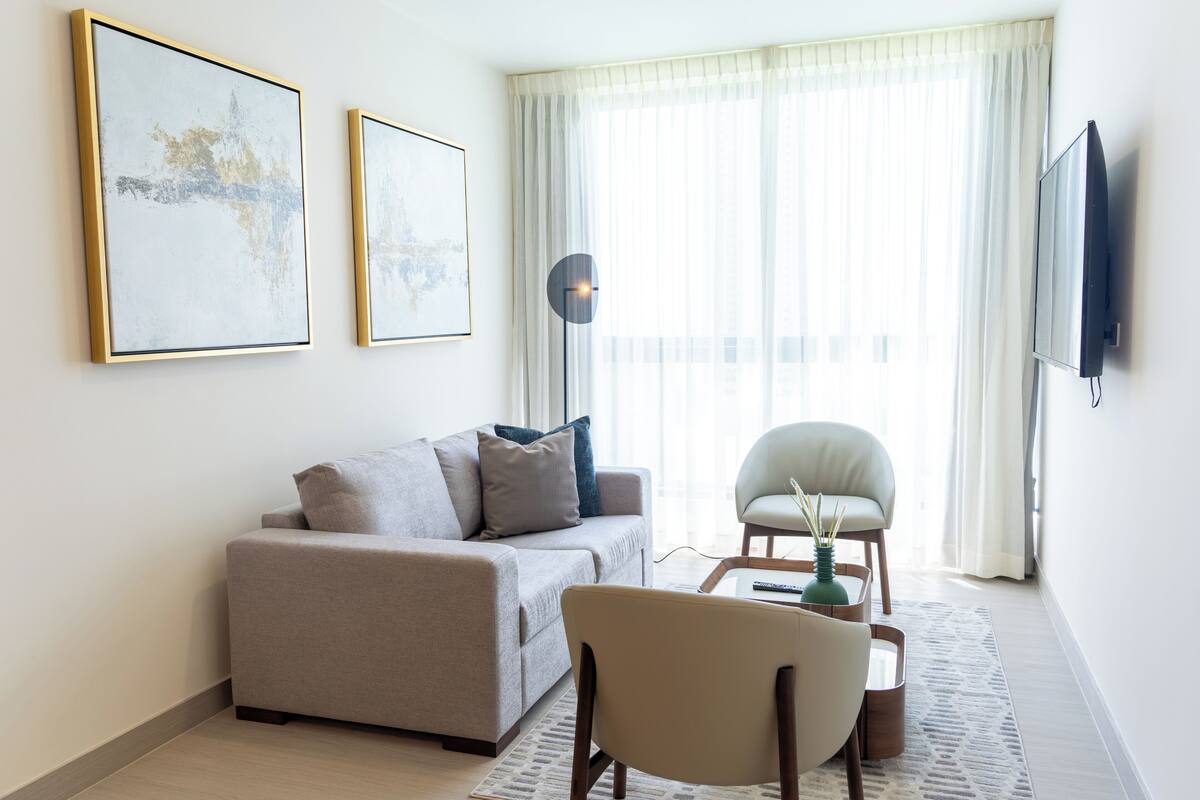 Een woonkamer met een bank, fauteuil, salontafel, vloerlamp en kunst aan de muur.
