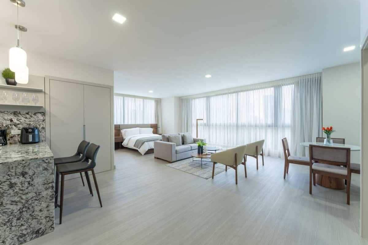 Una habitación de hotel moderna con una isla de cocina de mármol, cama con vistas, comedor y sala de estar.