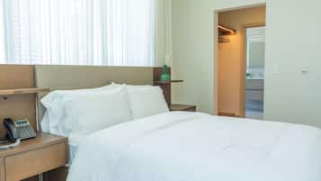 A hotel room with a bed, a bedside phone, a nightstand, and a window with curtains.