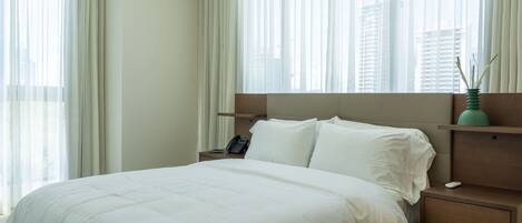 Une chambre d’hôtel avec un grand lit, une table de chevet, un téléphone et un vase contenant des roseaux.