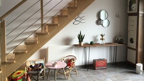 A staircase with wooden railings, a hanging light fixture, a small table with chairs, a potted plant, a vintage radio, and a clock on the wall. - Maison 3 Bord de Mer, Chez Ty Suzanne à 150m des Plages de Sable fin (Cléder)