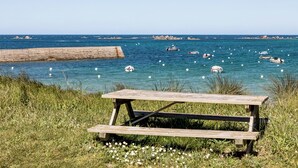 A wooden picnic table in a grassy area with a view of the sea and boats. - Maison 3 Bord de Mer, Chez Ty Suzanne à 150m des Plages de Sable fin (Cléder)