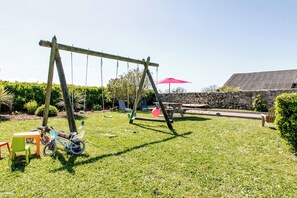 A backyard with a swing set, a picnic table, and a stone wall. - Maison 3 Bord de Mer, Chez Ty Suzanne à 150m des Plages de Sable fin (Cléder)