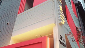 Un bâtiment moderne à la façade rouge et blanche bien visible, doté d’une grande fenêtre en verre et d’une enseigne avec du texte en coréen.