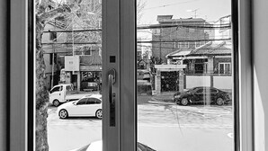 Une vue à travers une fenêtre avec une porte, donnant sur une scène de rue avec des voitures et des bâtiments.