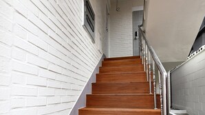Un escalier avec des marches en bois et des rampes en métal, menant à un palier avec un mur en briques blanches et une porte.