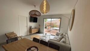 A modern living room with a wooden dining table, a sofa, and a TV mounted on the wall. - Magnifique Appartement Neuf, 3 ch 6 p Centre Ville Avec Jardin Calme et Lumineux (Sainte-Maxime)