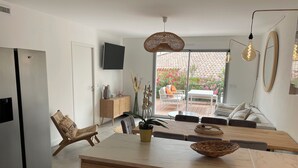 A modern kitchen with a wooden island, a dining area with a table and chairs, a sofa, and a view of a garden through large windows. - Magnifique Appartement Neuf, 3 ch 6 p Centre Ville Avec Jardin Calme et Lumineux (Sainte-Maxime)