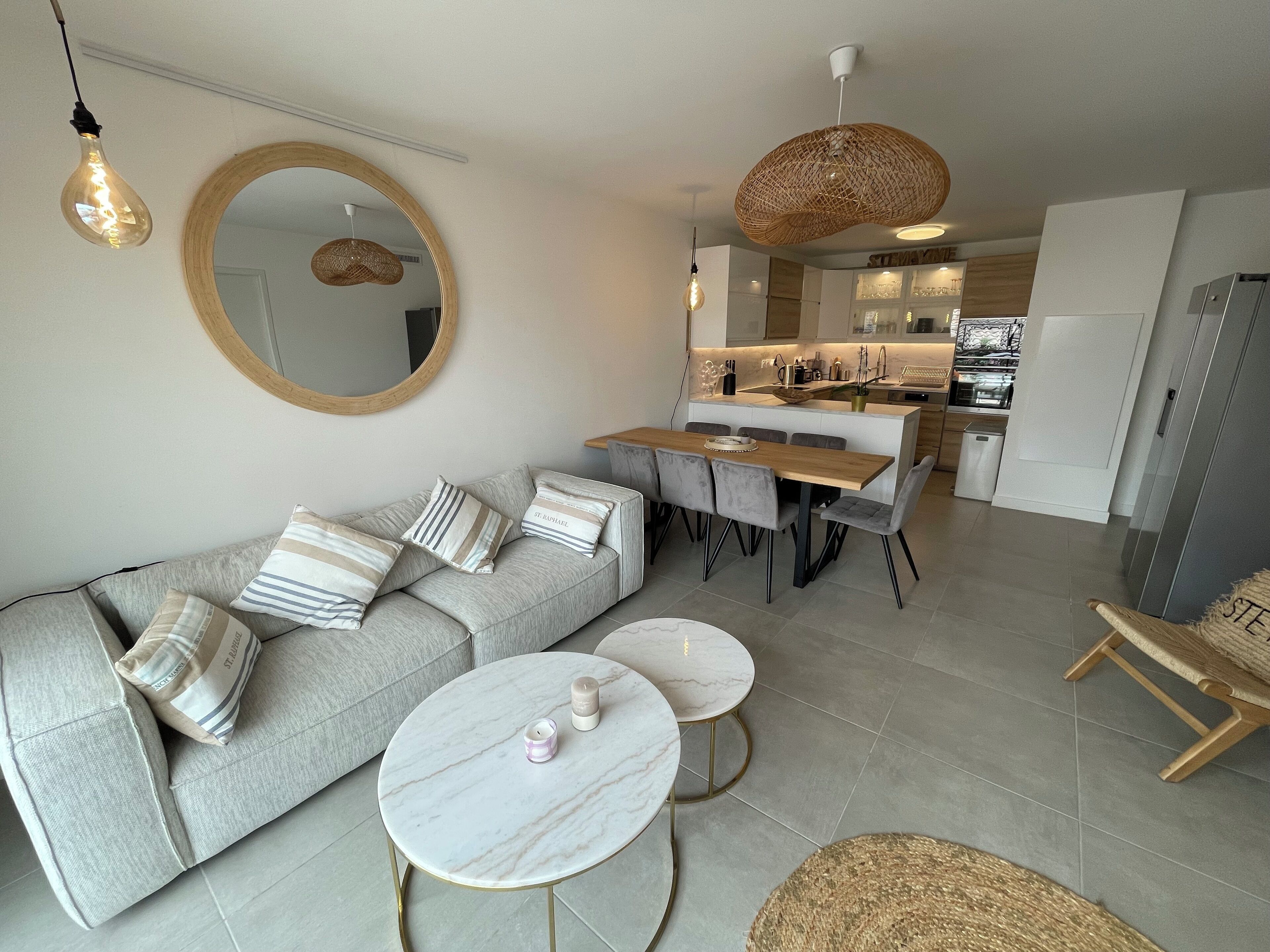 A modern living room with a grey sofa, round coffee table, and a dining area with a wooden table and chairs.