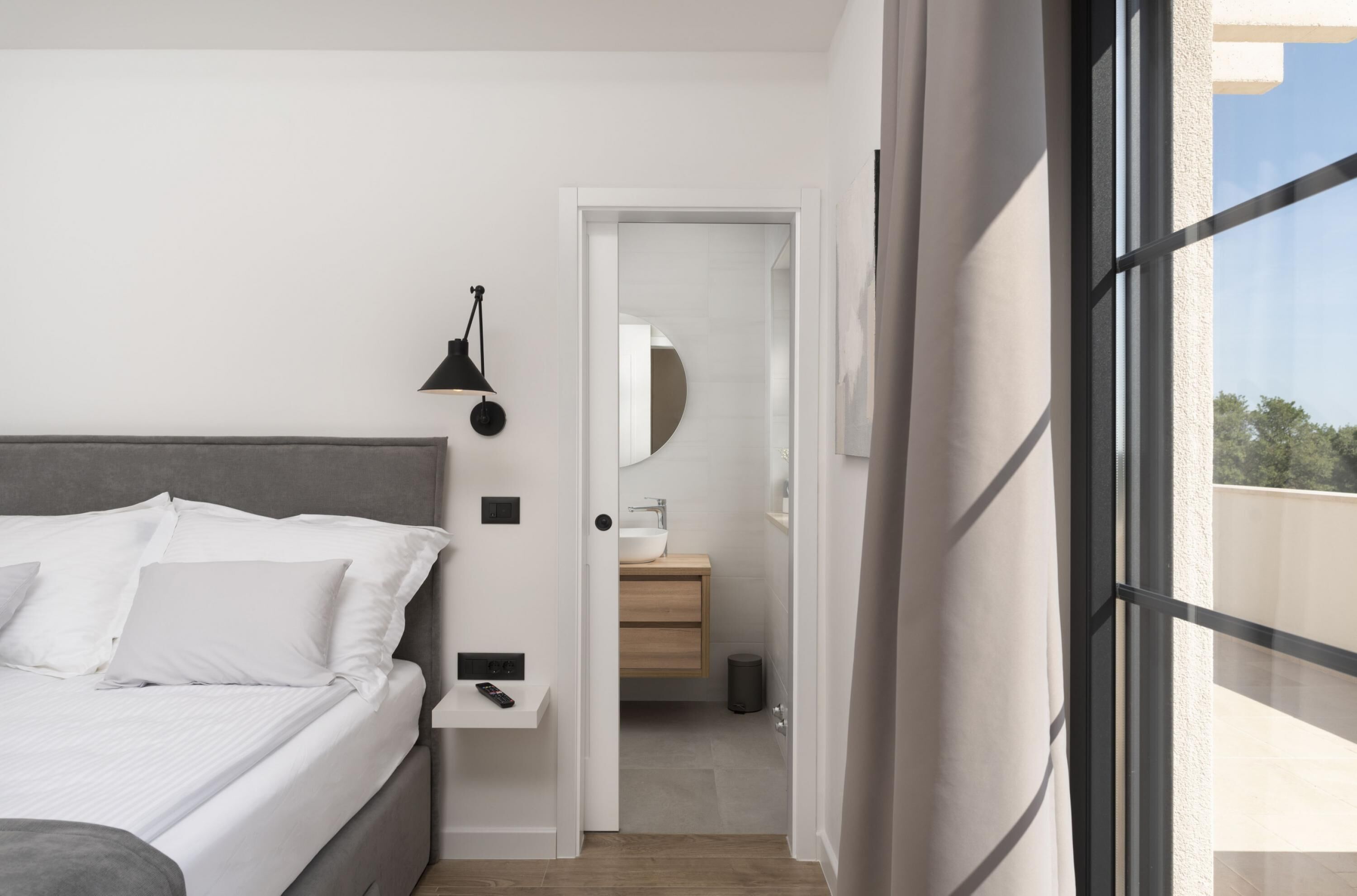 Ein modernes Schlafzimmer mit Bett, Nachttisch und Blick ins Badezimmer durch eine geöffnete Tür.