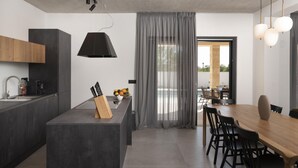 Une cuisine moderne dotée d’un îlot central, d’un coin repas avec une table et des chaises en bois, et offrant une vue sur l’extérieur grâce à de grandes fenêtres.