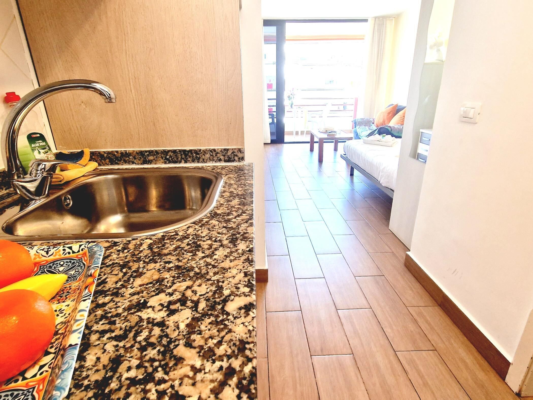 A kitchen with a stainless steel sink, a granite countertop, and a patterned mat.