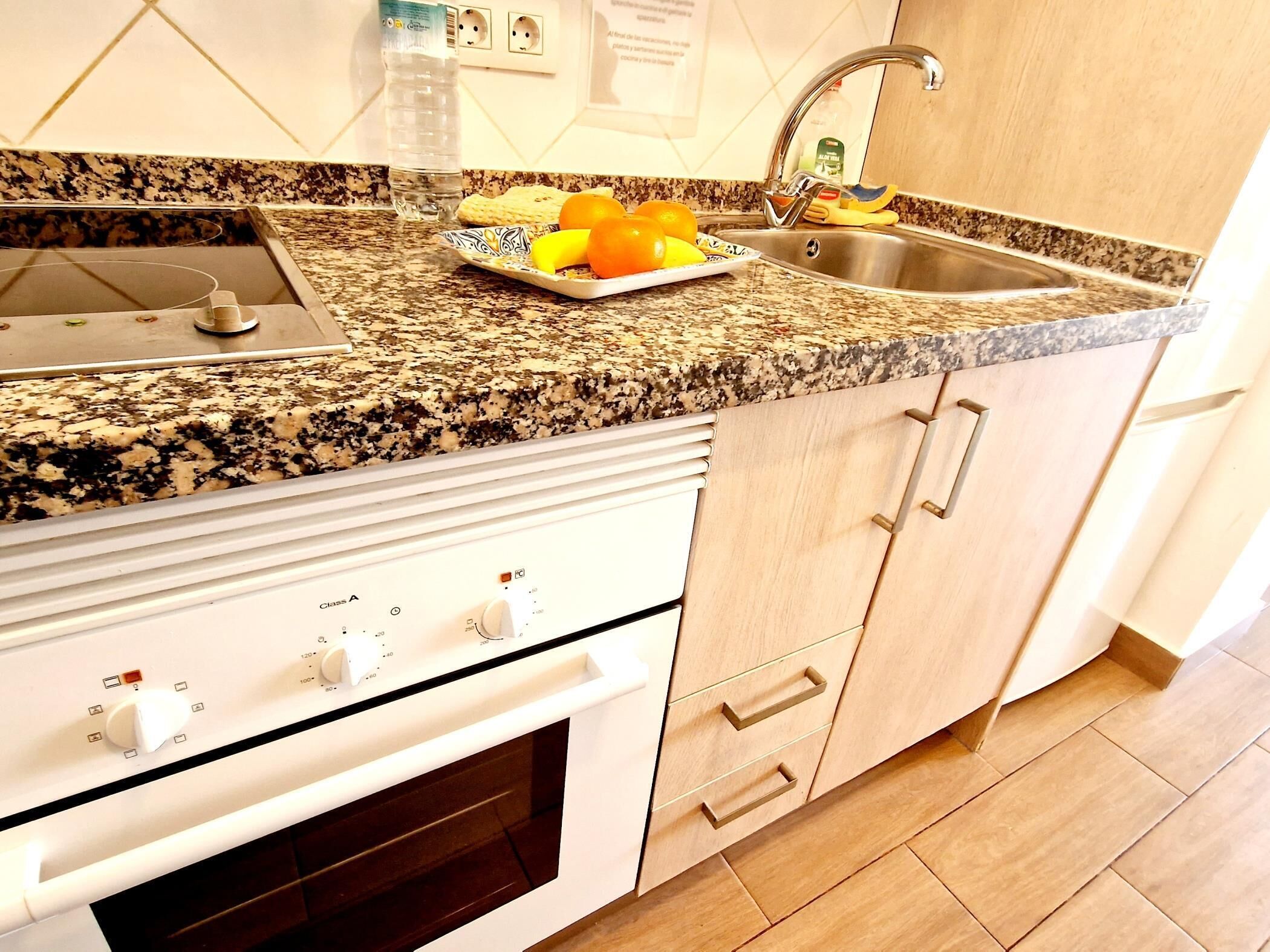 Una cocina con encimeras de granito, pileta de acero inoxidable y horno integrado.