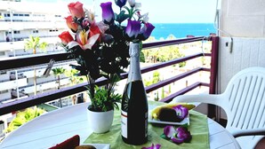 A balcony with a table set for a meal, a bottle of wine, and a vase of flowers. - OLYMPIA STUDIO OCEAN VIEW (Playa de las Américas)