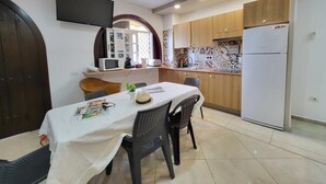 Une cuisine compacte dotée d’appareils électroménagers modernes, un coin repas avec une table et des chaises, et un téléviseur fixé au mur.