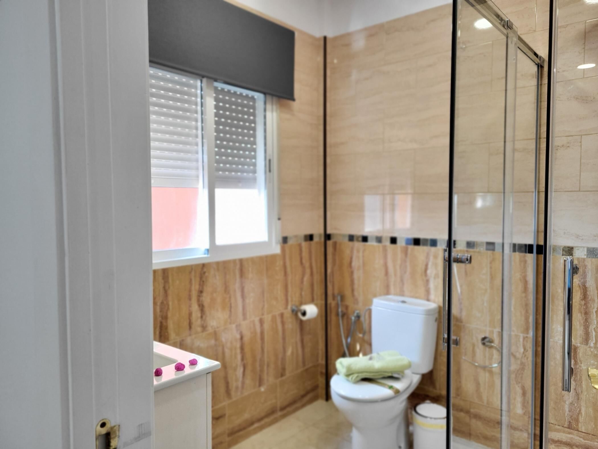 A modern bathroom with a toilet, shower, and a window with blinds.