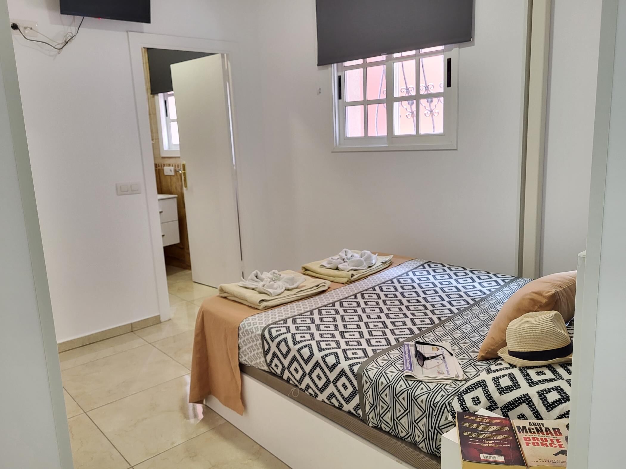 Een slaapkamer met een bed, een raam, een televisie en een deur naar een badkamer.