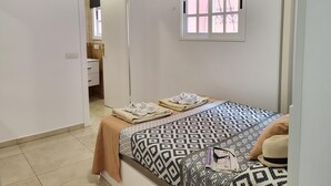 Ein Schlafzimmer mit einem Bett, einem an der Wand befestigten Fernseher, einem Fenster und einer Tür zu einem Badezimmer.
