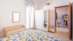 A bedroom with a bed, a wardrobe, a mirror, and a door leading to a kitchen area. - 3870 Casa del Pescador by Barbarhouse (Vieste)