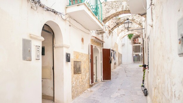 A narrow street with buildings on either side, featuring arched doorways and a bicycle parked against a wall. - 3870 Casa del Pescador by Barbarhouse (Vieste)
