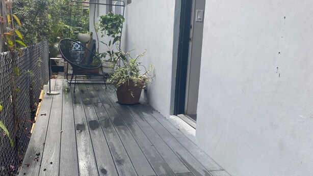 Une terrasse en bois avec un pot de fleurs et une chaise, un mur blanc et une porte.