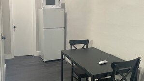 Une petite cuisine compacte, équipée d’un réfrigérateur et d’un four à micro-ondes, une table à manger en bois foncé avec des chaises, et une porte donnant sur une autre pièce.