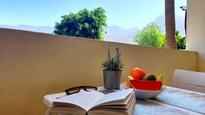 A balcony with a table, a book, a pair of glasses, a potted plant, and a bowl of fruit. - Mareverde Resort, Blue Studio (Costa Adeje)