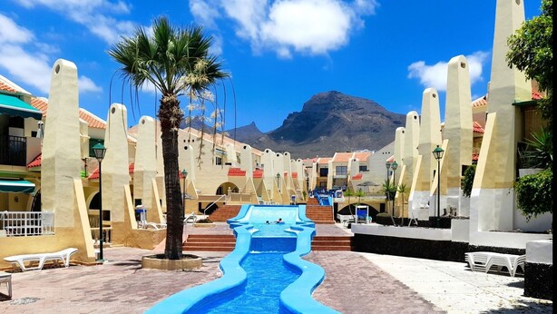 A pool area with a blue water slide, palm trees, and steps leading to a pool. - Mareverde Resort, Blue Studio (Costa Adeje)