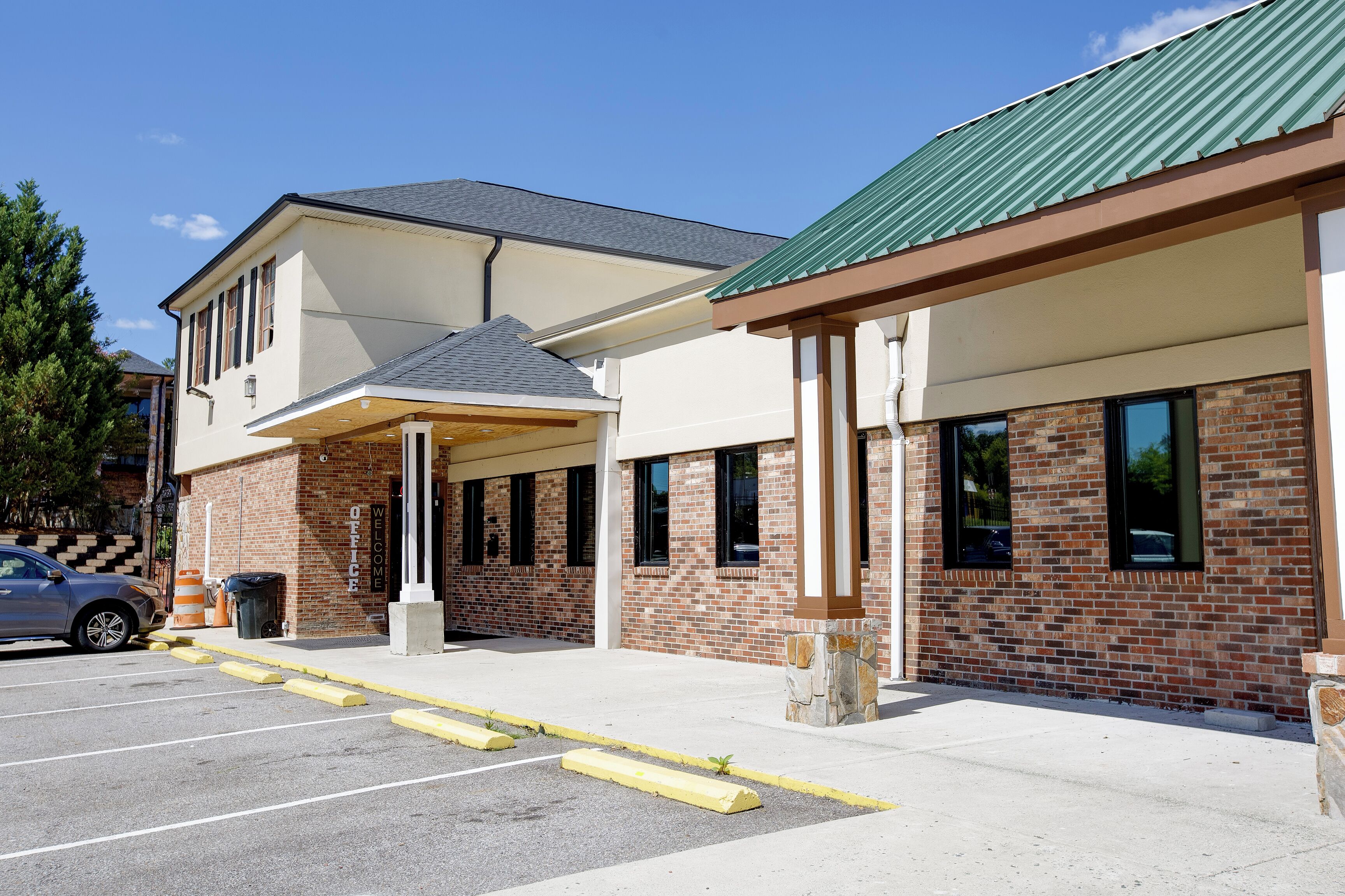 A hotel entrance with a covered waiting area, a parking lot, and a brick facade.
