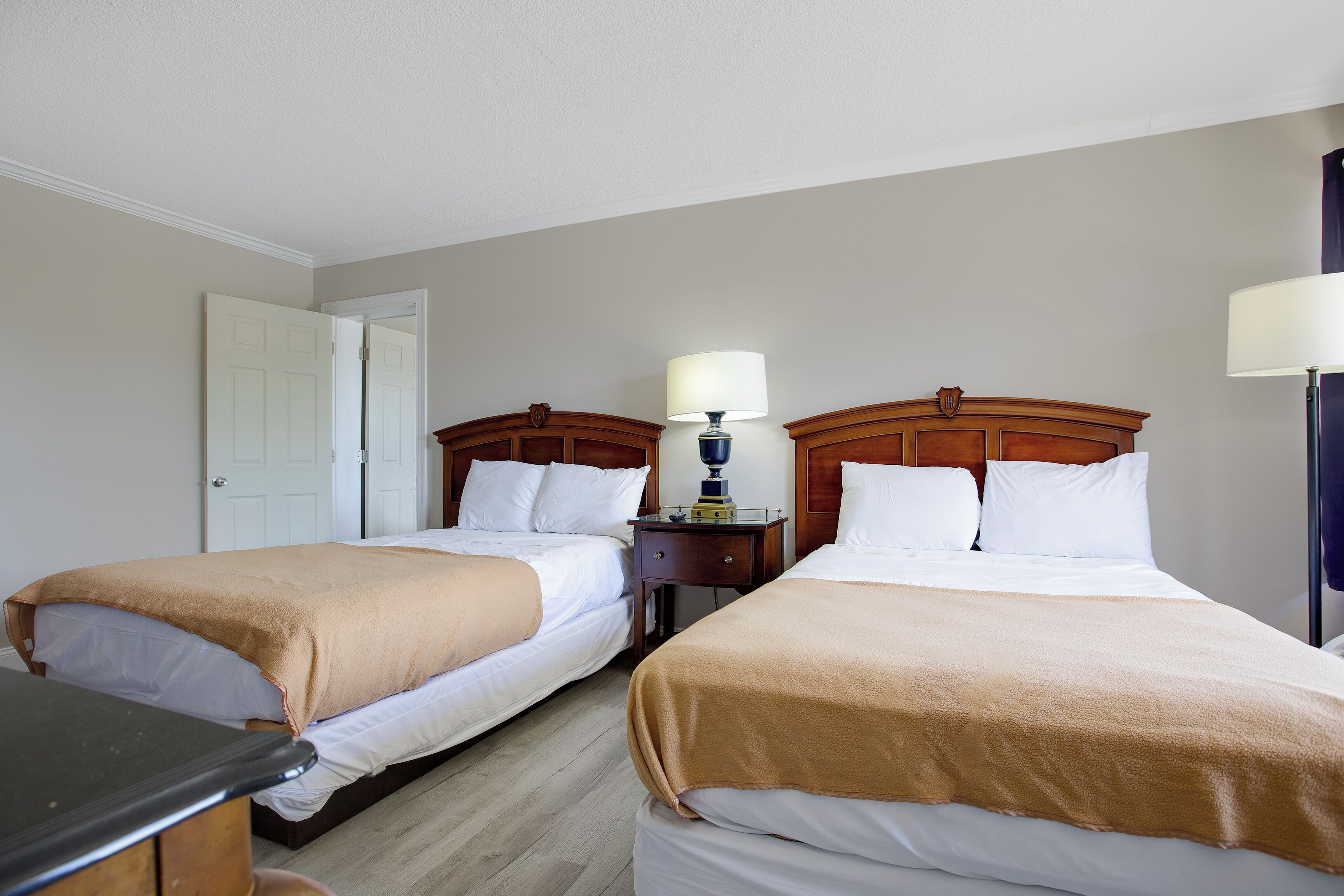 A hotel room with two single beds, a nightstand with a lamp, and a door.