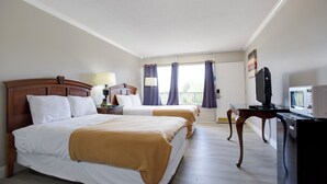 Habitación de hotel con dos camas, televisión, escritorio con computadora y ventana con cortinas.