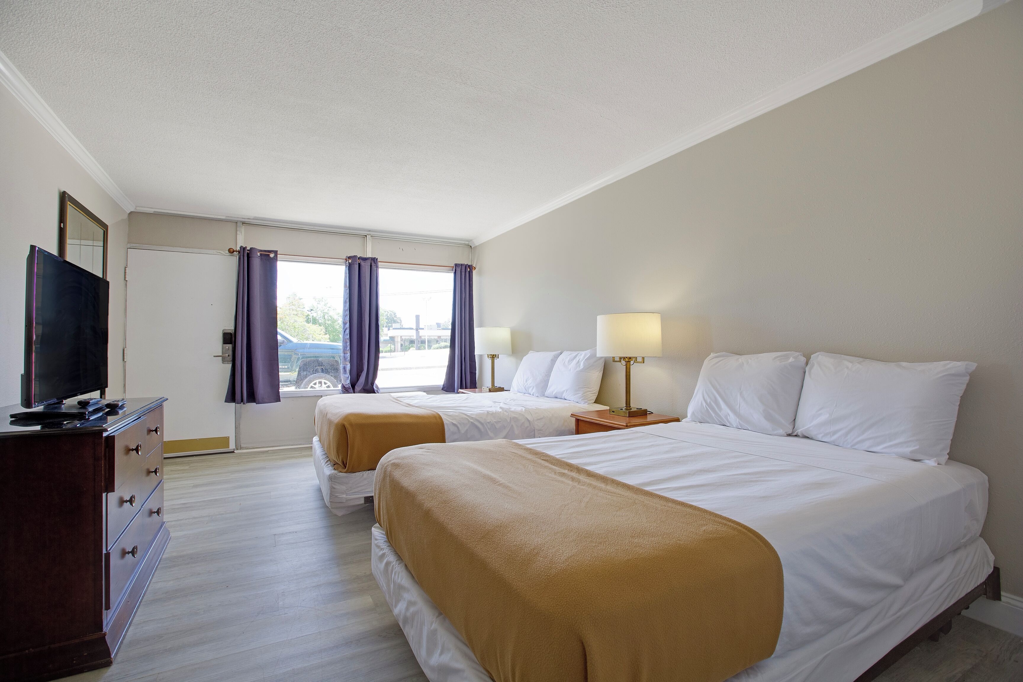 Une chambre d’hôtel avec deux lits, une télévision, un bureau et une fenêtre avec des rideaux.