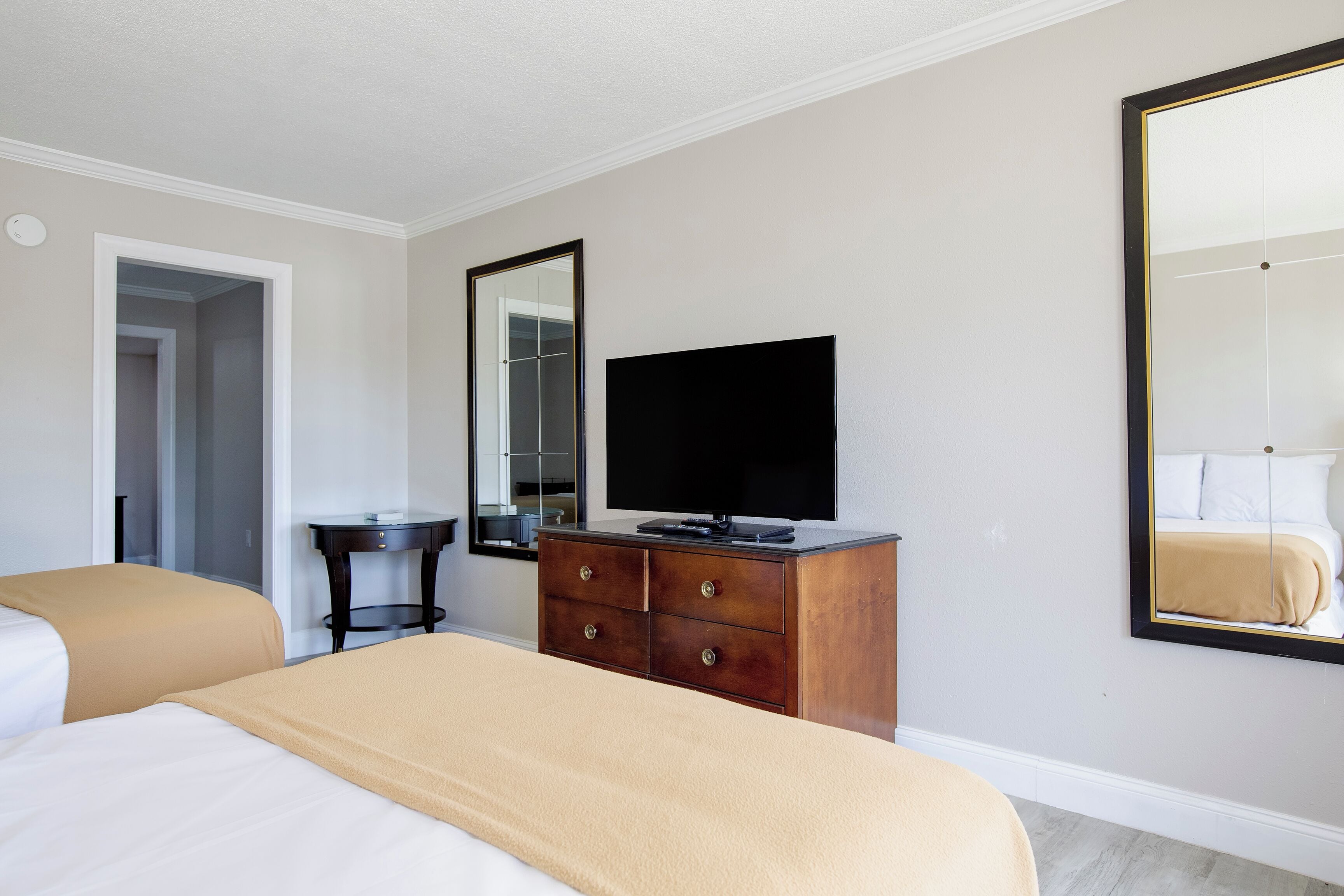 Habitación de hotel con dos camas, un tocador, un televisor y un espejo grande.