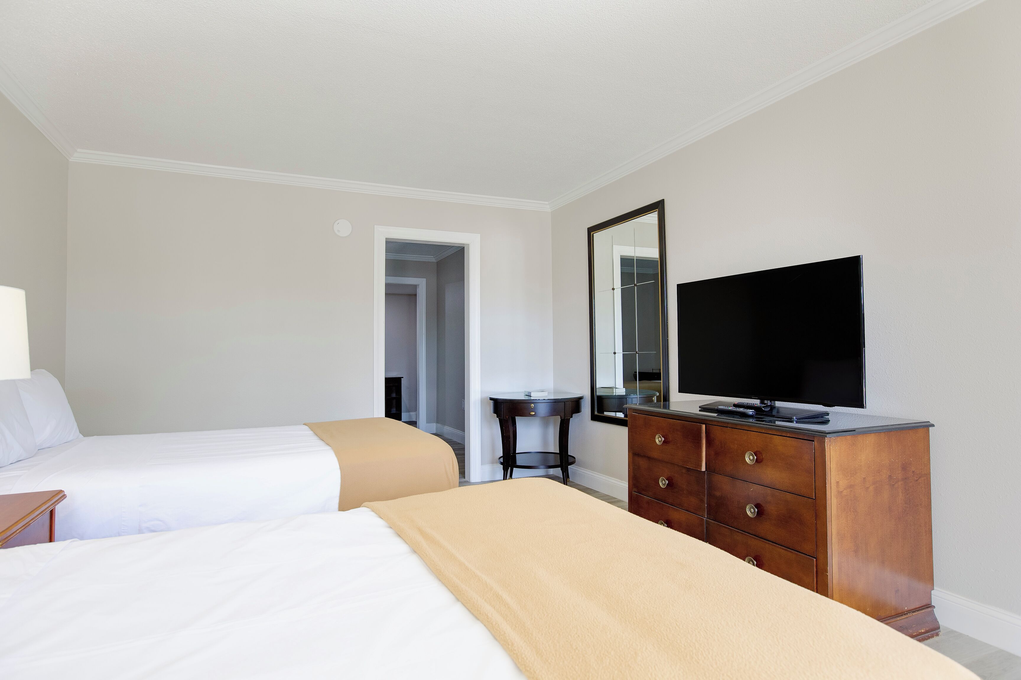 Une chambre d’hôtel avec deux lits, une commode, un téléviseur et une porte donnant sur une autre pièce.