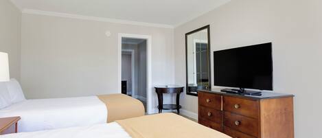 Een hotelkamer met twee bedden, een kaptafel, een televisie en een deur naar een andere kamer.