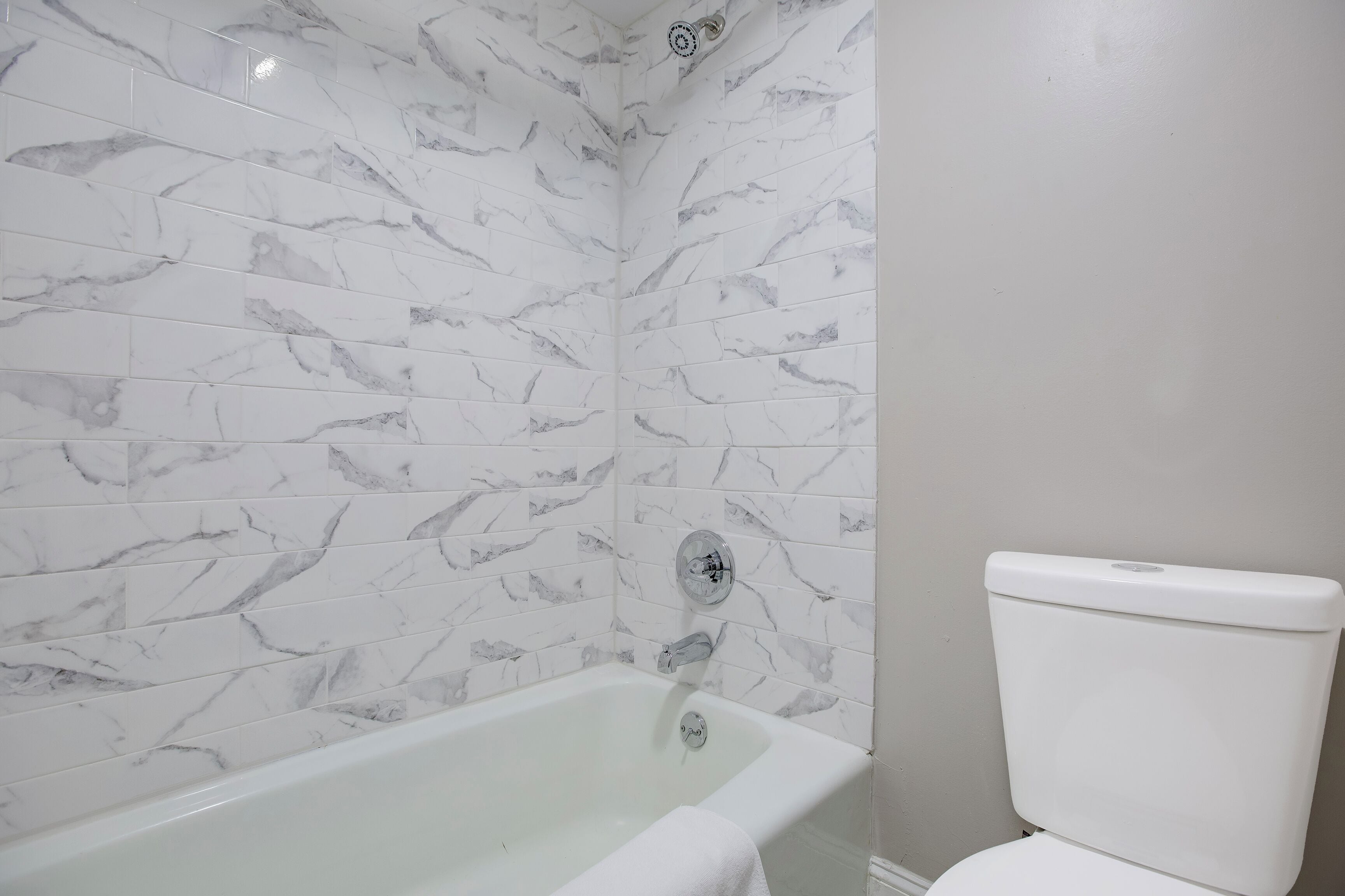 A bathroom with a bathtub, a toilet, and marble-patterned walls.