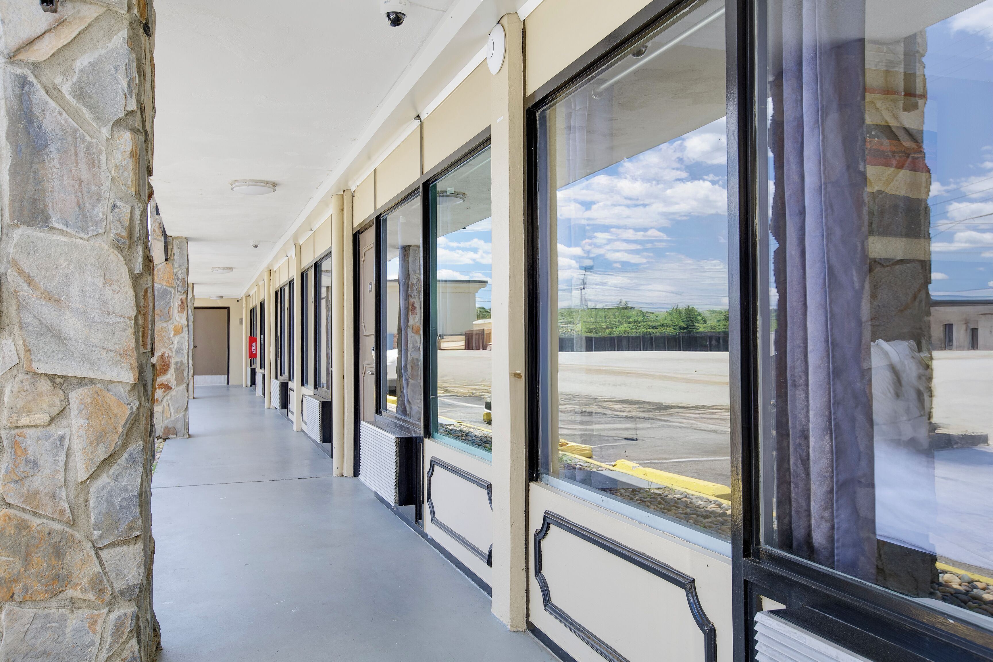 A corridor with stone walls and large windows, leading to a parking area.