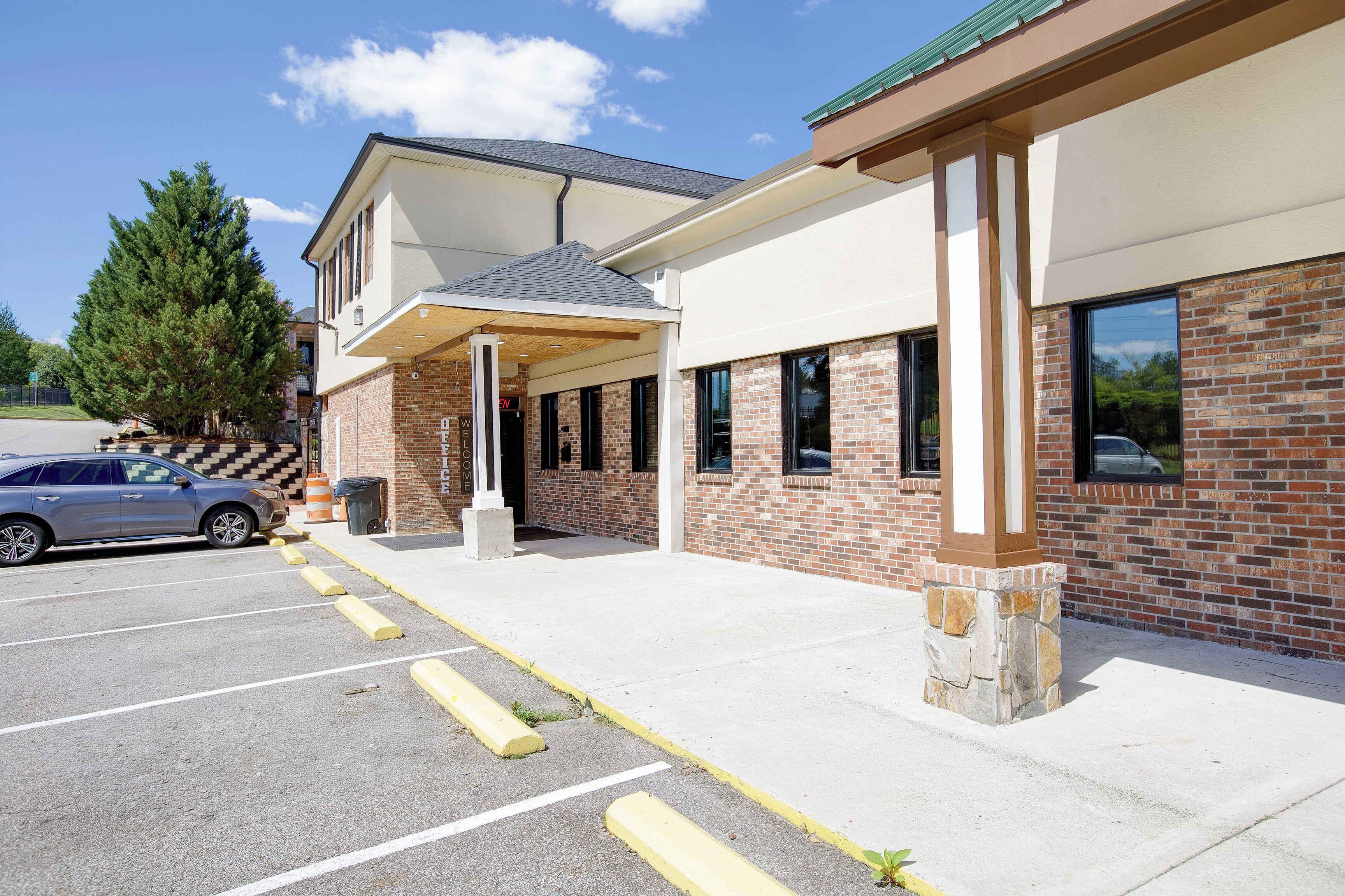 A building with a brick facade, a covered entrance, and a parking lot with marked spaces.