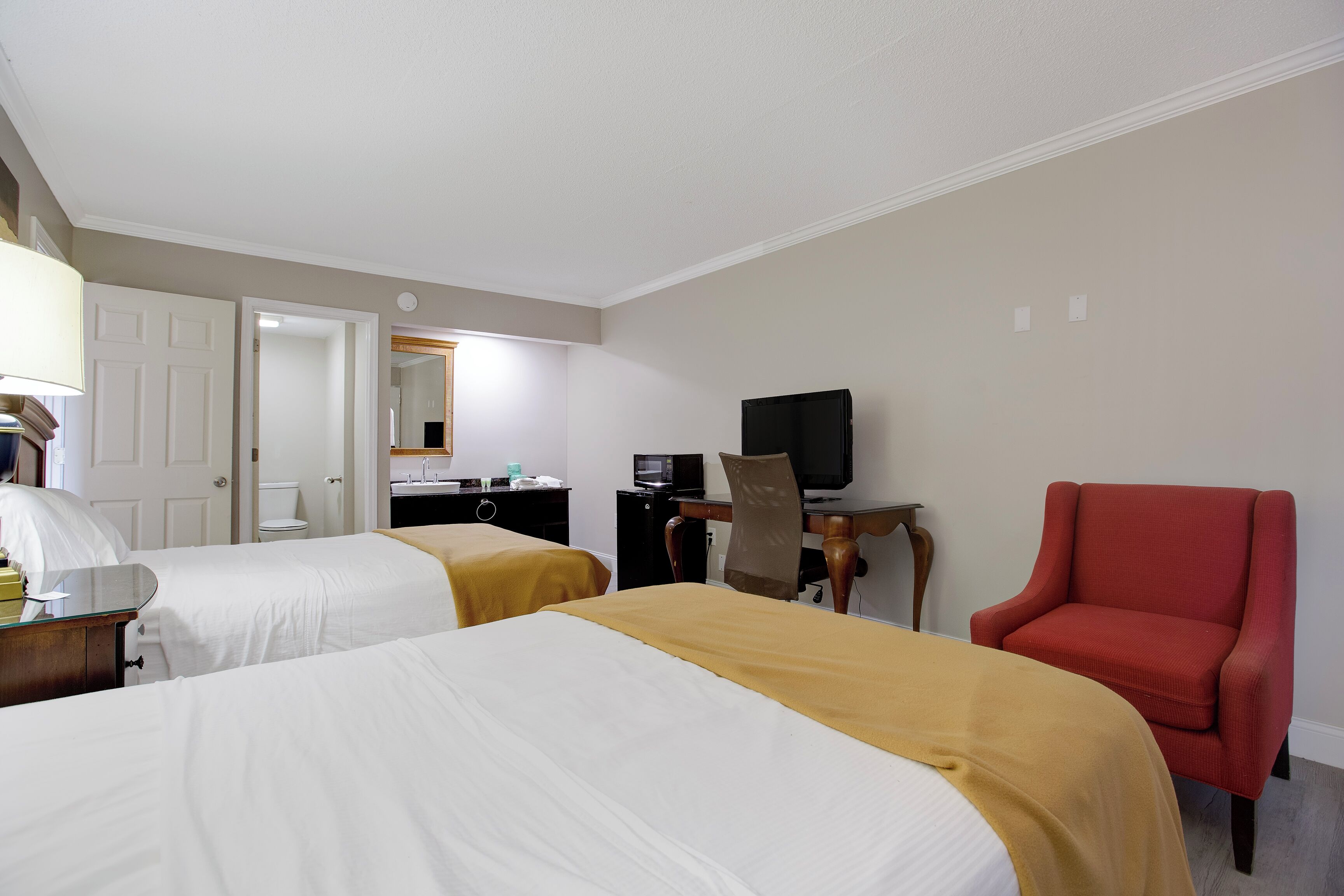 A hotel room with two beds, a desk with a computer, a television, and a red armchair.