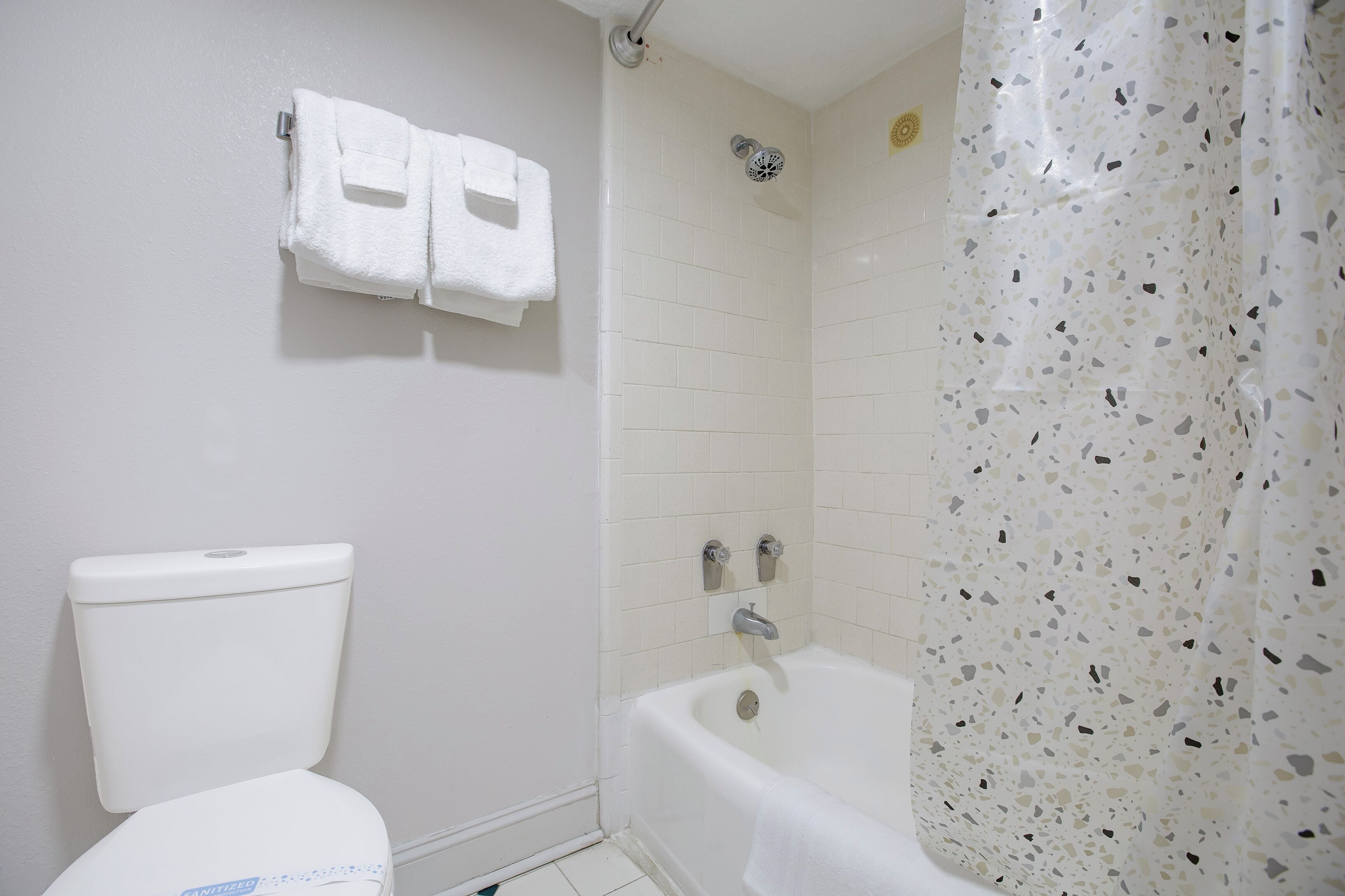 Un baño con inodoro, ducha con cortina salpicada y toallero de pared.