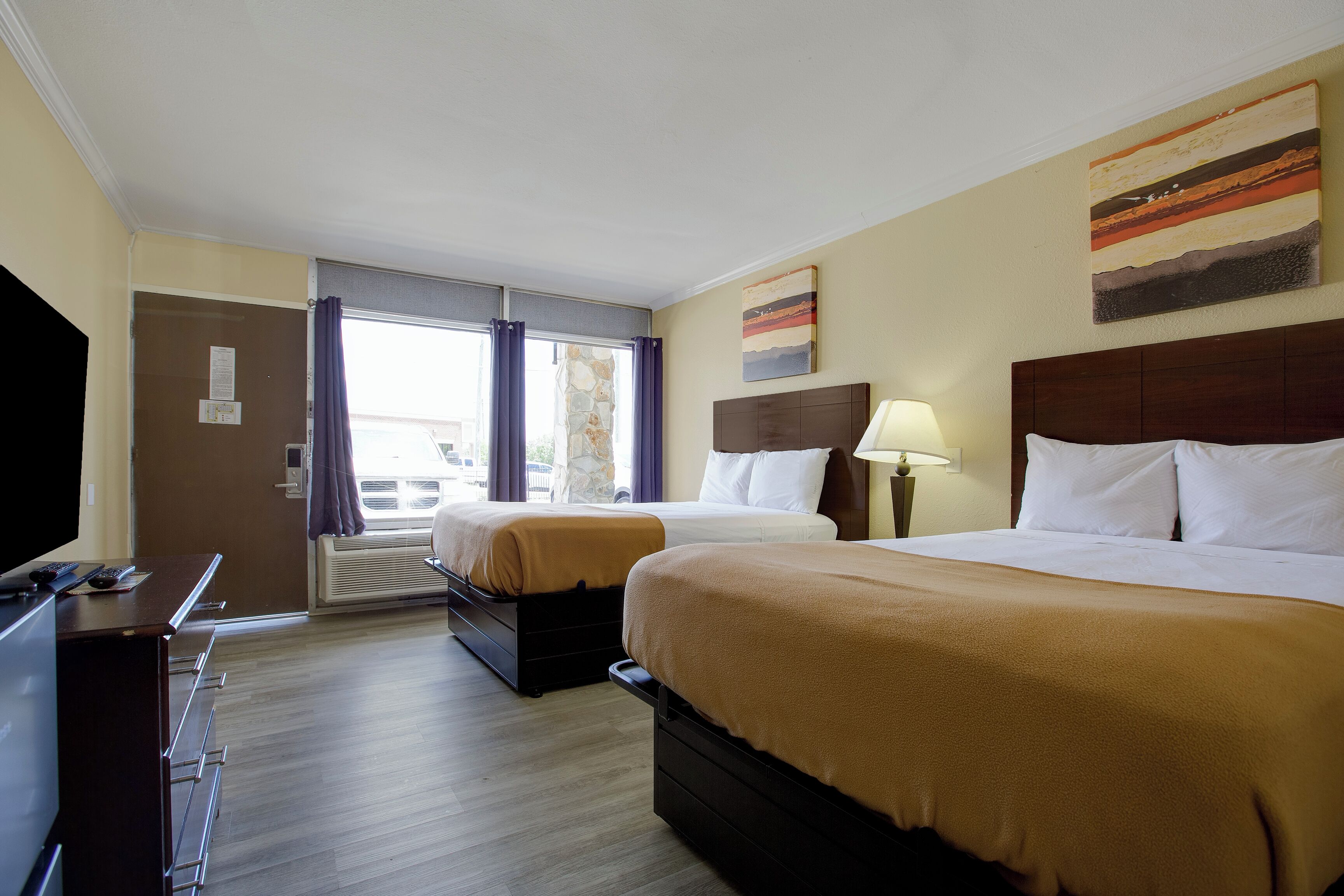A hotel room with two beds, a desk, a TV, and a window with curtains.