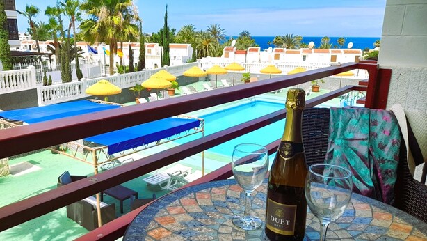 Un balcon donnant sur une piscine, une bouteille de vin Duet Brut et deux verres posés sur une table carrelée.